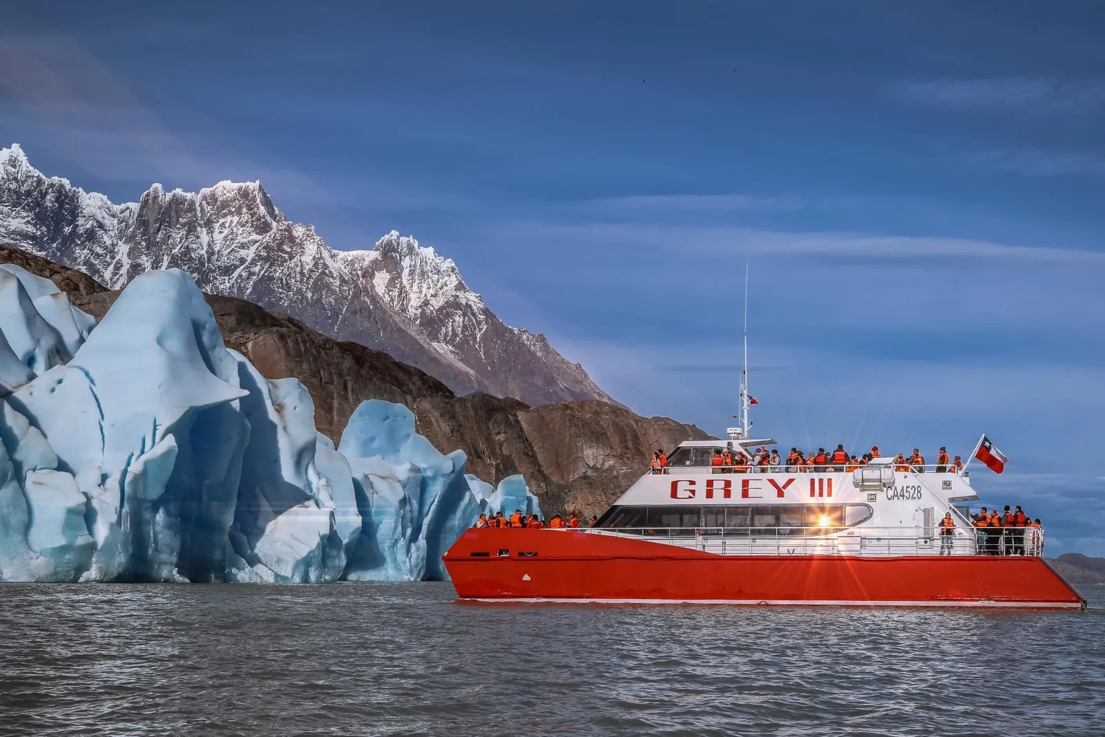 The catamaran beneath glacier ice and snowy peaks