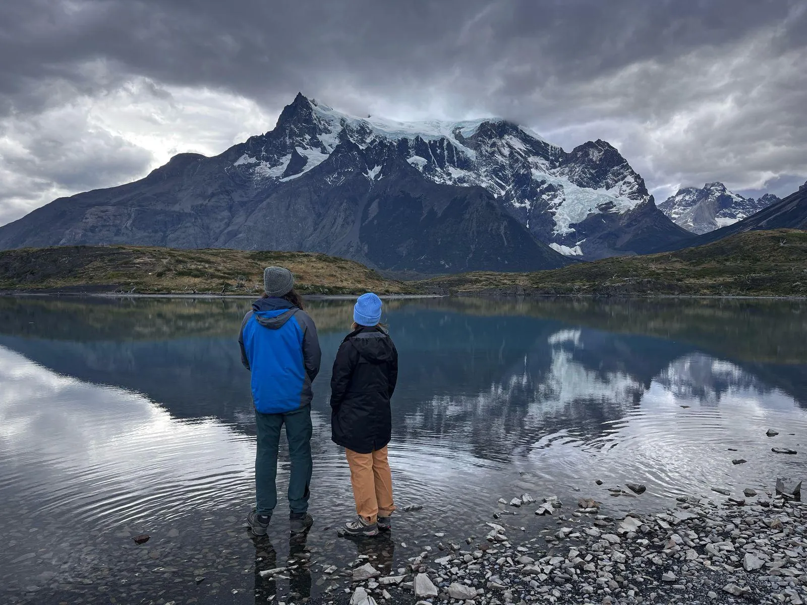 Two hikers on a lakeshore reflecting Paine Grande