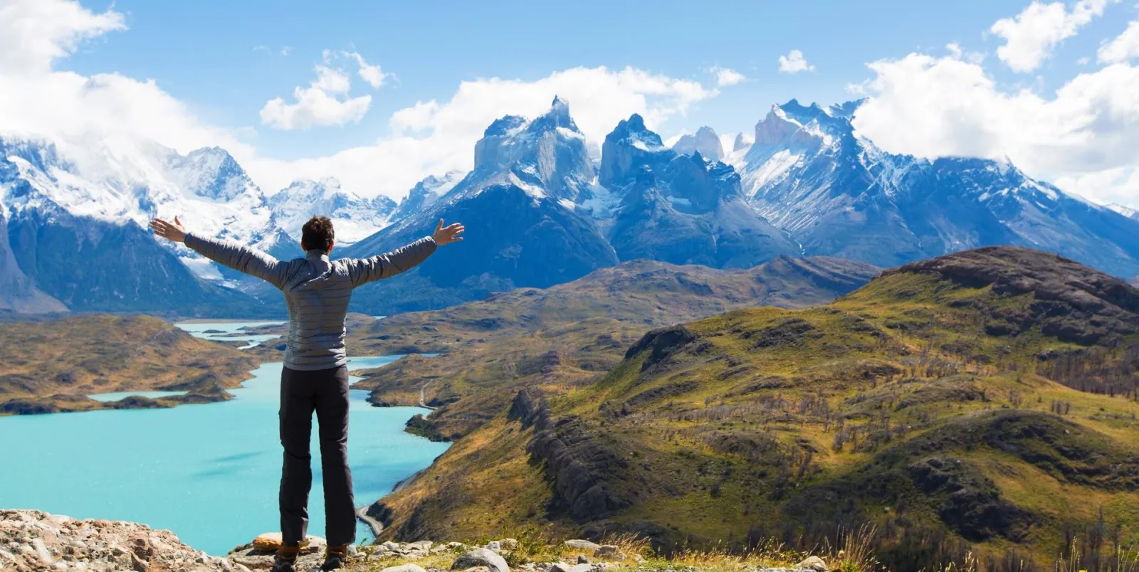 Traveller with arms raised above turquoise Lake Pehoé