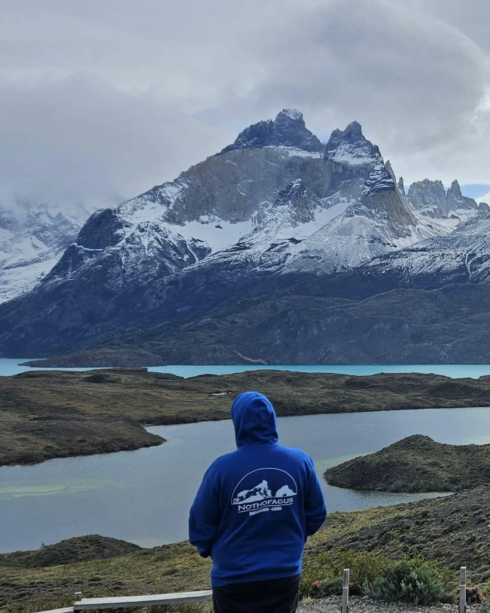 Traveller overlooking a turquoise lake below snowy peaks