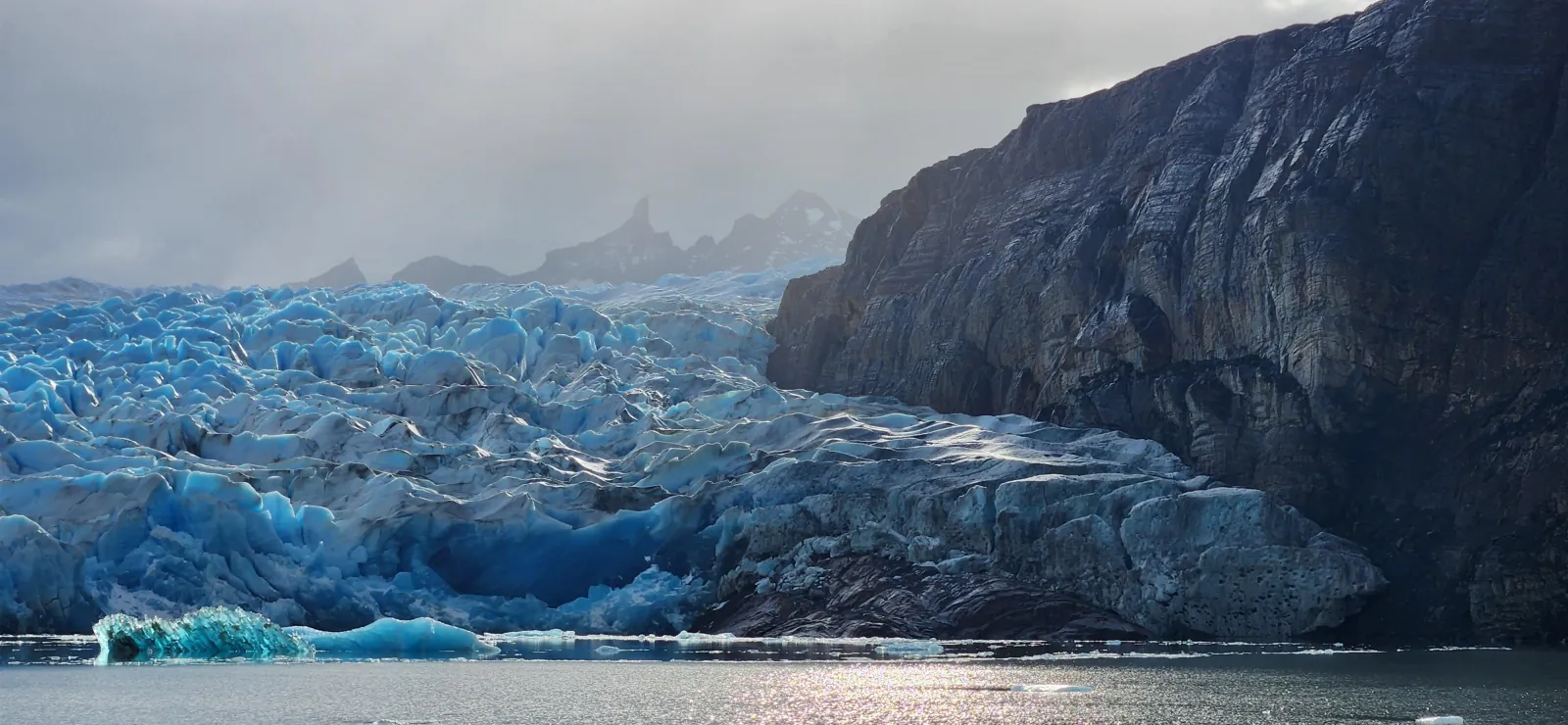 The ice face of Grey Glacier beside dark rock walls